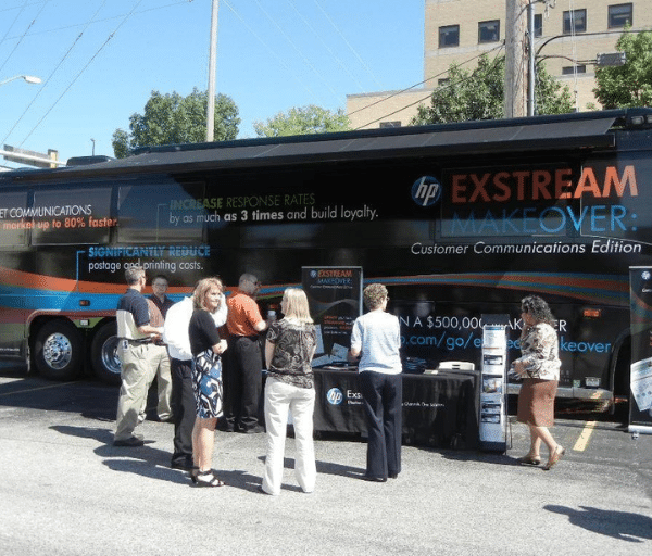A group of women waiting in front of an HP Extream Makeover mobile roadshow trailer and table display.