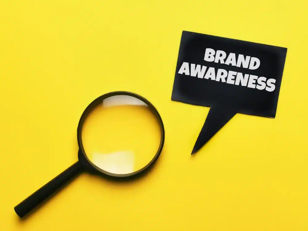 Top view of a technology concept; magnifying glass with brand awareness in a speech bubble on a yellow background