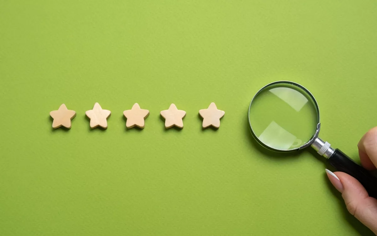Concept photo; five stars on a green background next to a hand holding a magnifying glass