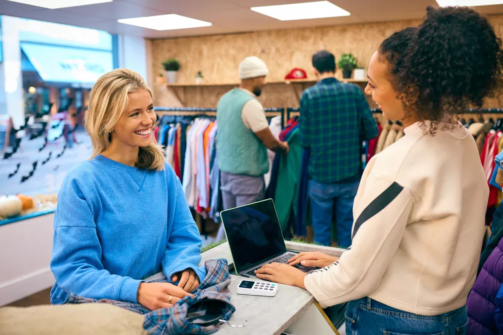 Woman Buying Shirt From Female Sales Assistant At Cash Desk In Fashion Store